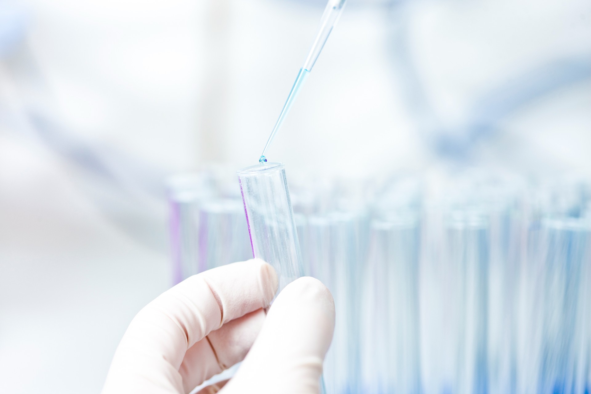 Vlear test tubes being picked up by a person wearing gloves