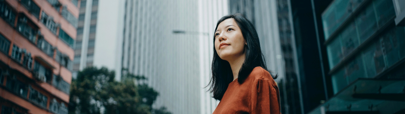 Low angle portrait of confidence young woman standing against highrise city buildings in city